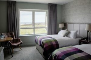 Tweepersoons hotelkamer met twee bedden, groot raam en uitzicht op open landschap.