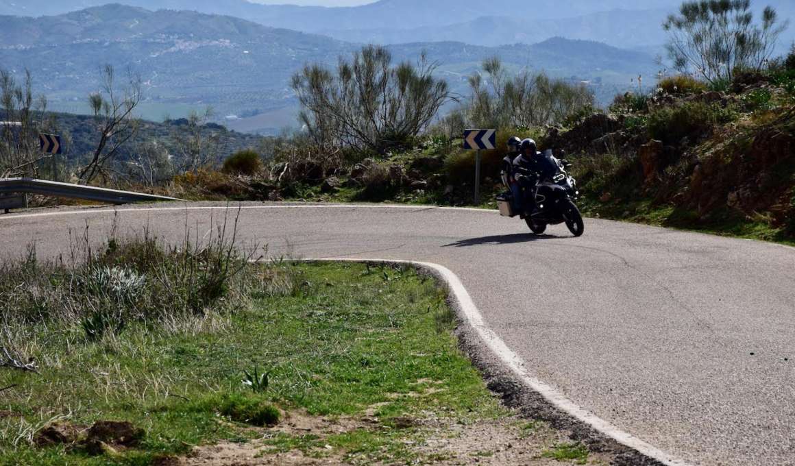 9 essentiële tips voor een geslaagde motorvakantie 15 Motorrijder met duopassagier op kronkelige weg in heuvelachtig landschap