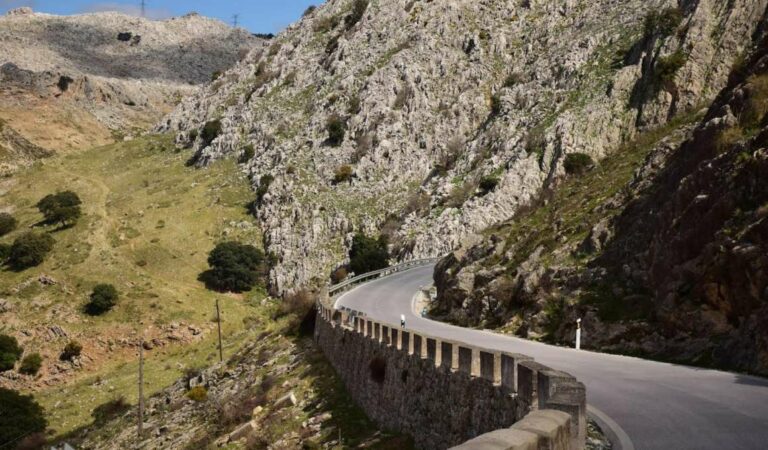 Bochtige asfaltweg langs een steile rotswand in bergachtig landschap