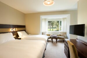 Ruime hotelkamer met meerdere bedden, zithoek bij het raam en uitzicht op groen buiten.