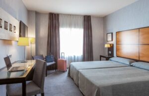 Hotelkamer met tweepersoonsbed, bureau, stoel en raam met daglicht