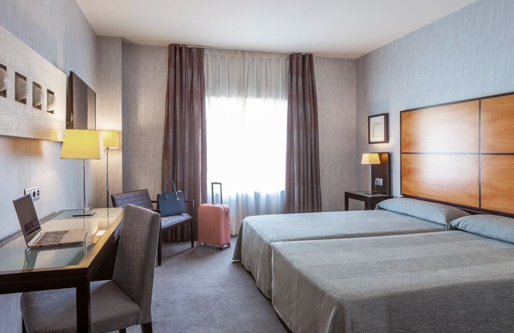Hotelkamer met tweepersoonsbed, bureau, stoel en raam met daglicht