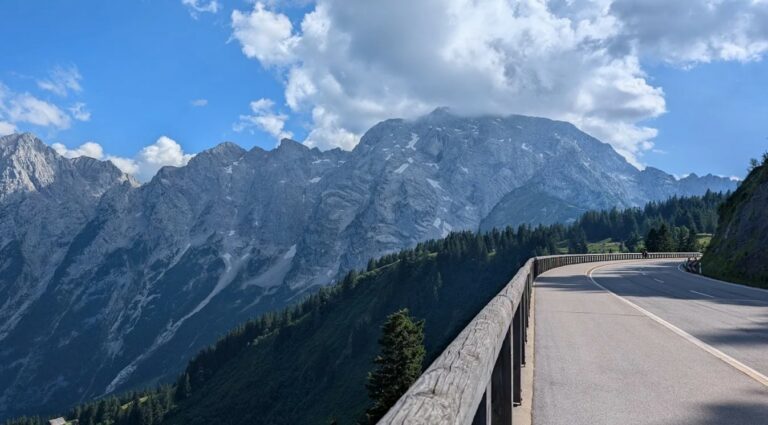 Bergweg met vangrail en indrukwekkend rotsachtig bergmassief op de achtergrond