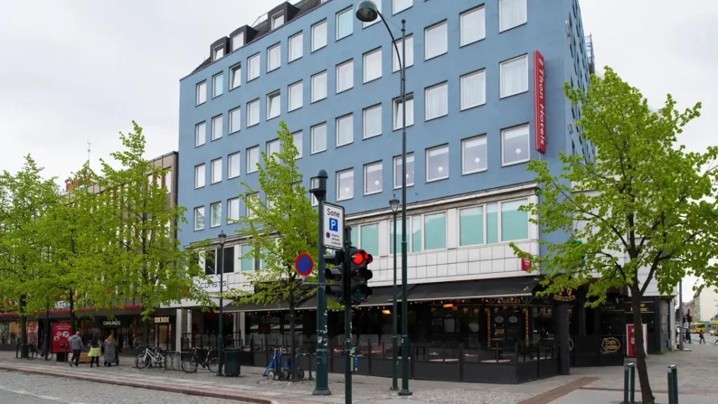 Groot hotelgebouw aan een straat met bomen en winkels
