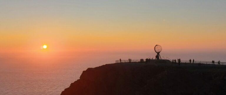Zonsondergang bij de Noordkaap met silhouetten van bezoekers en de wereldbol