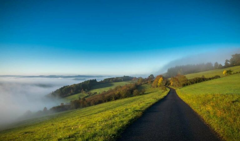Smalle weg door heuvelachtig landschap in de Eifel met laaghangende bewolking